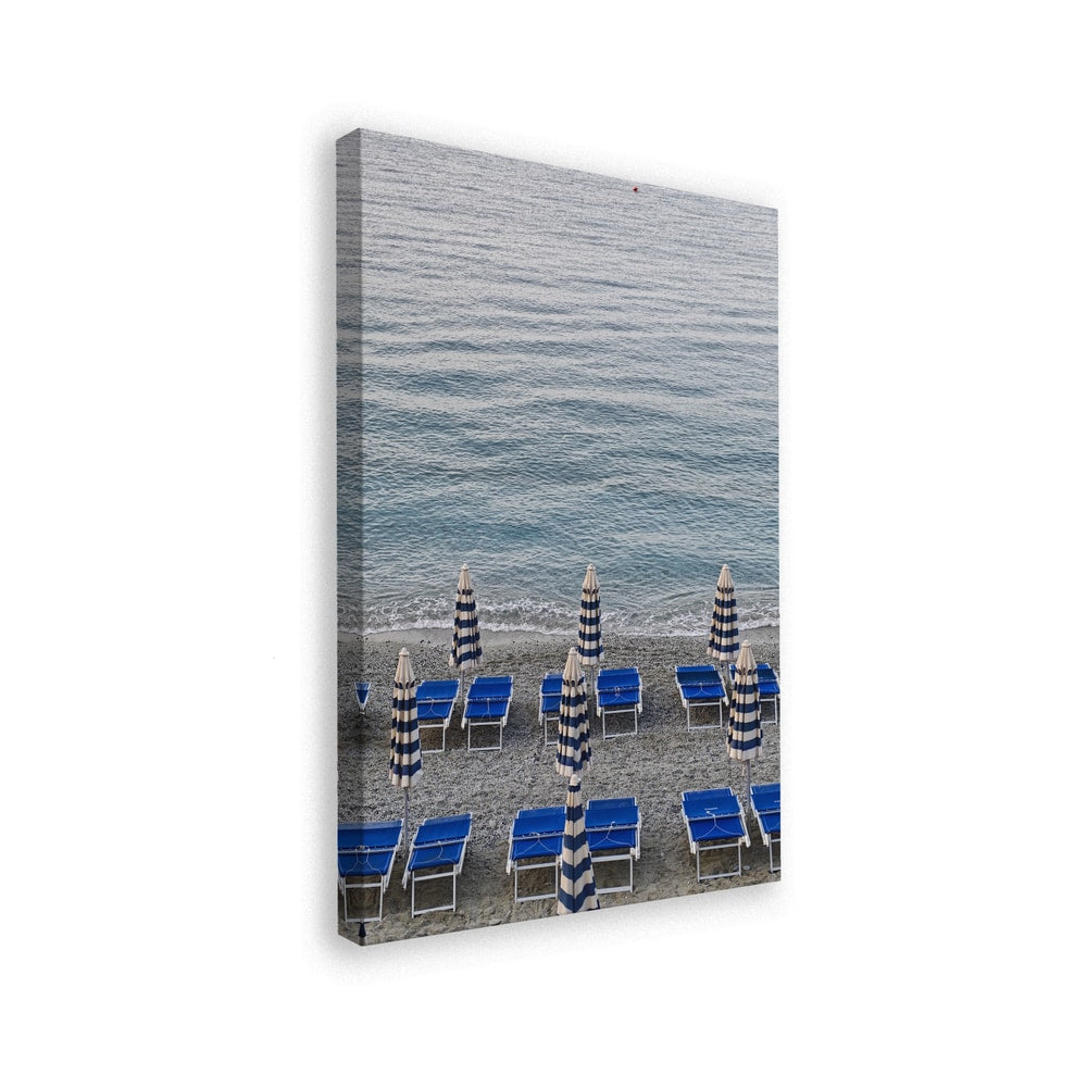 Blaue Strandliegen und geschlossene gestreifte Sonnenschirme am Kiesstrand vor dem Meer
