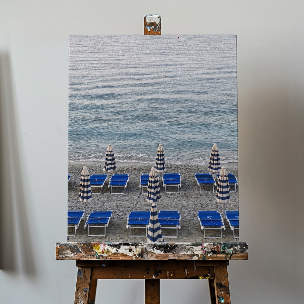 Blaue Strandliegen und geschlossene gestreifte Sonnenschirme am Kiesstrand vor dem Meer
