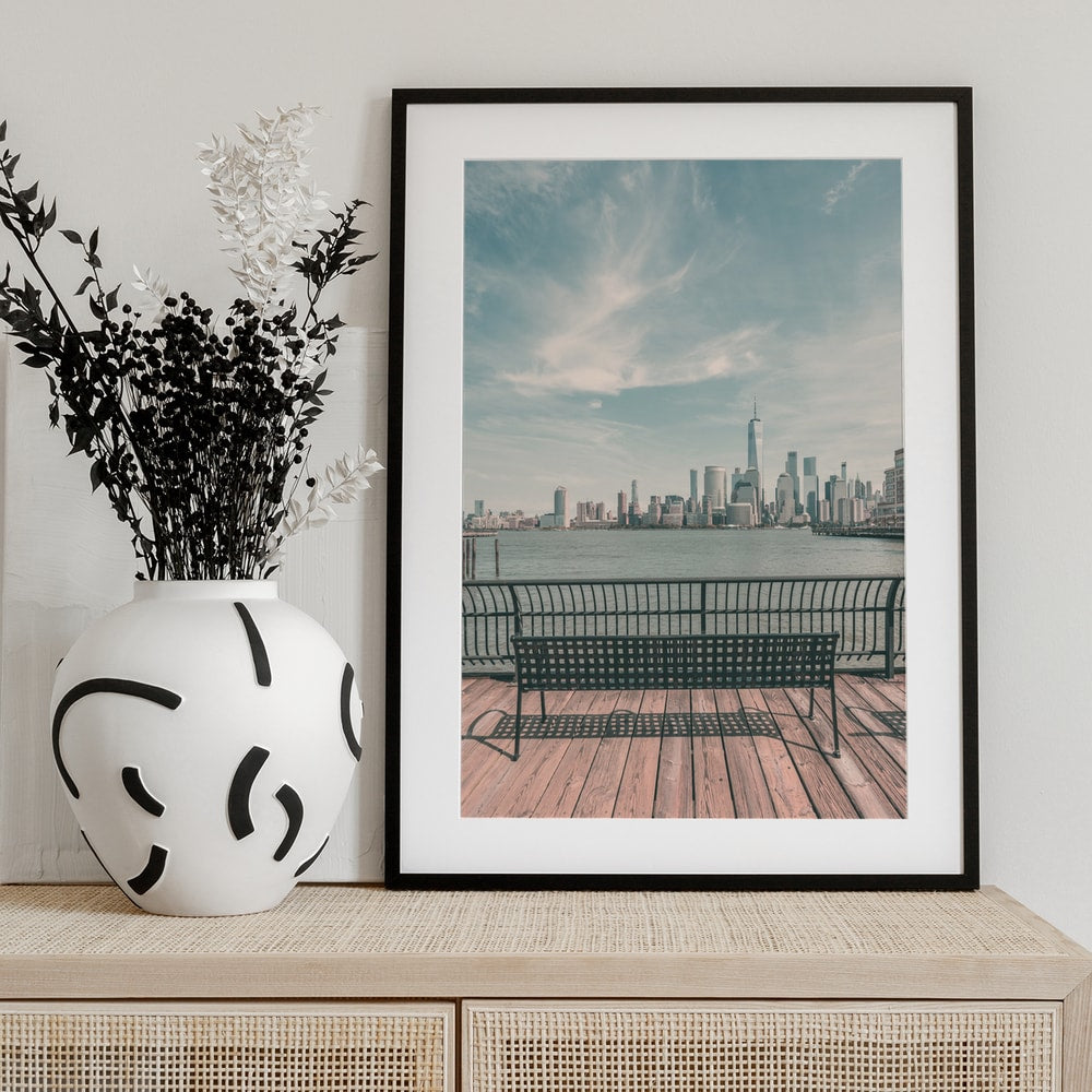 Fotografie einer Bank auf einem Holzpier mit der Skyline von Manhattan im Hintergrund