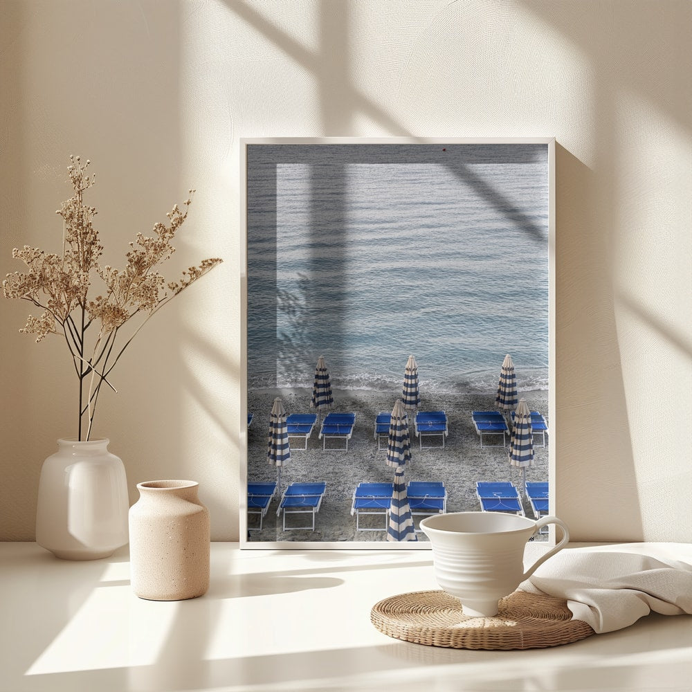Blaue Strandliegen und geschlossene gestreifte Sonnenschirme am Kiesstrand vor dem Meer