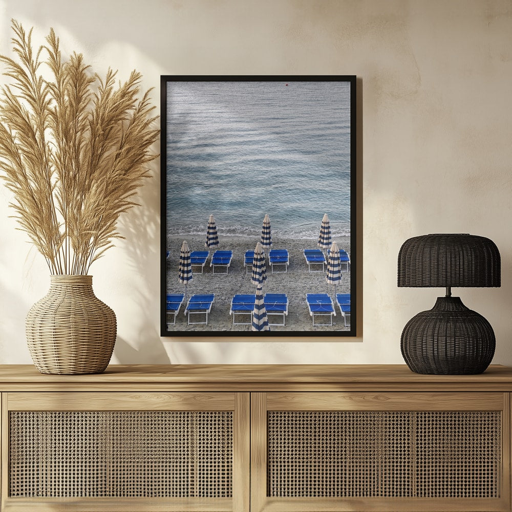 Blaue Strandliegen und geschlossene gestreifte Sonnenschirme am Kiesstrand vor dem Meer
