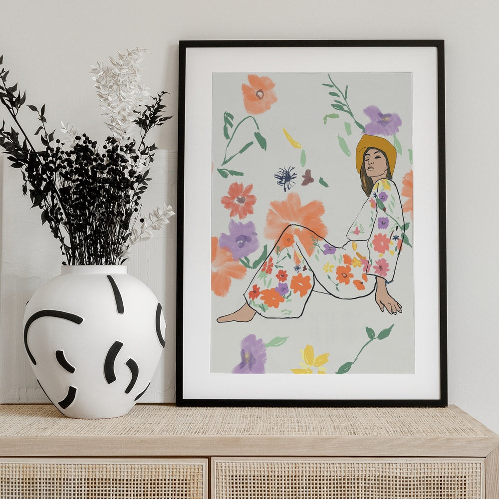 Illustration einer sitzenden Frau mit gelbem Hut im Blumenkleid zwischen bunten Blüten