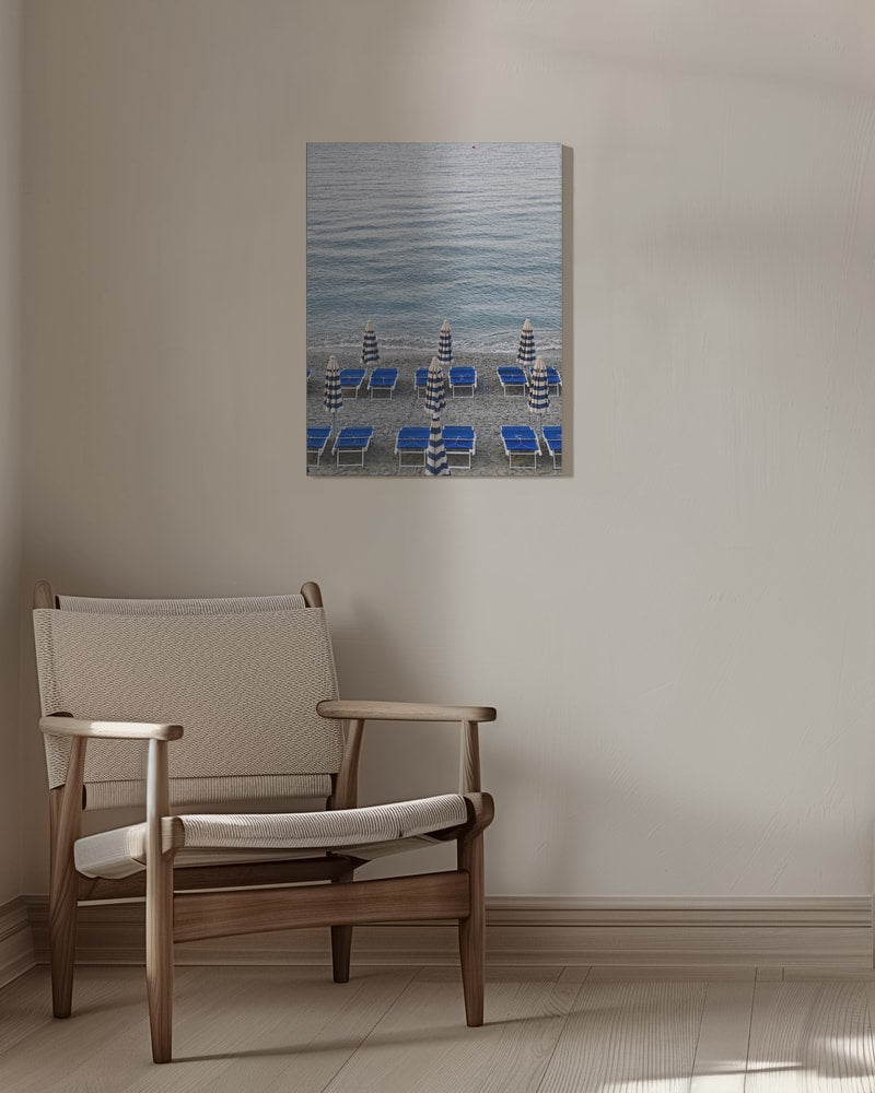 Blaue Strandliegen und geschlossene gestreifte Sonnenschirme am Kiesstrand vor dem Meer