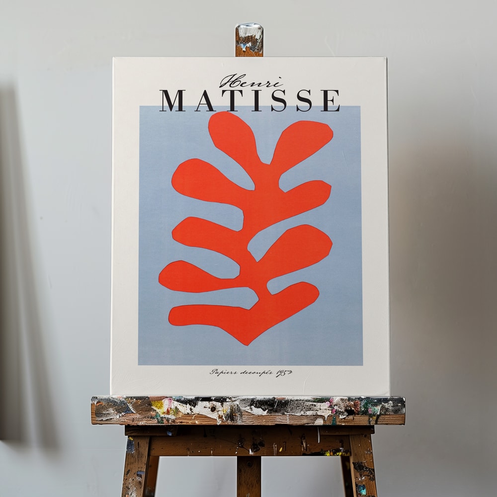 Ausstellungsplakat Henri Matisse mit korallenrotem Scherenschnitt-Blatt auf hellblauem Grund, schwarzer Schriftzug