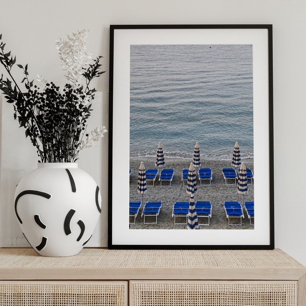 Blaue Strandliegen und geschlossene gestreifte Sonnenschirme am Kiesstrand vor dem Meer